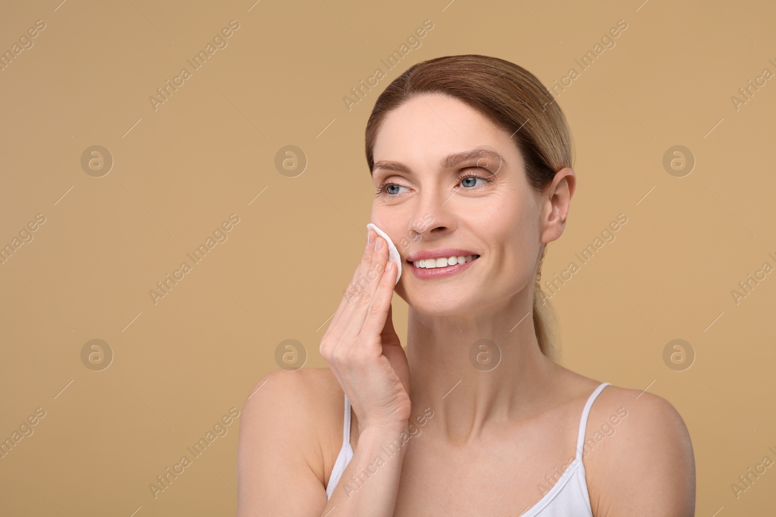 Photo of Beautiful woman removing makeup with cotton pad on beige background, space for text