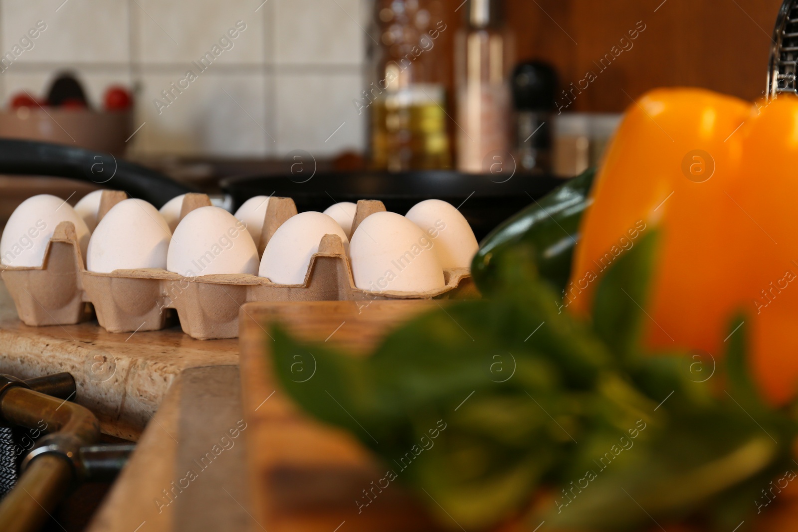 Photo of Many fresh eggs in carton and bell pepper on wooden countertop in kitchen. Ingredients for breakfast