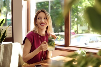 Young woman with mason jar of tasty natural lemonade in cafe. Detox drink