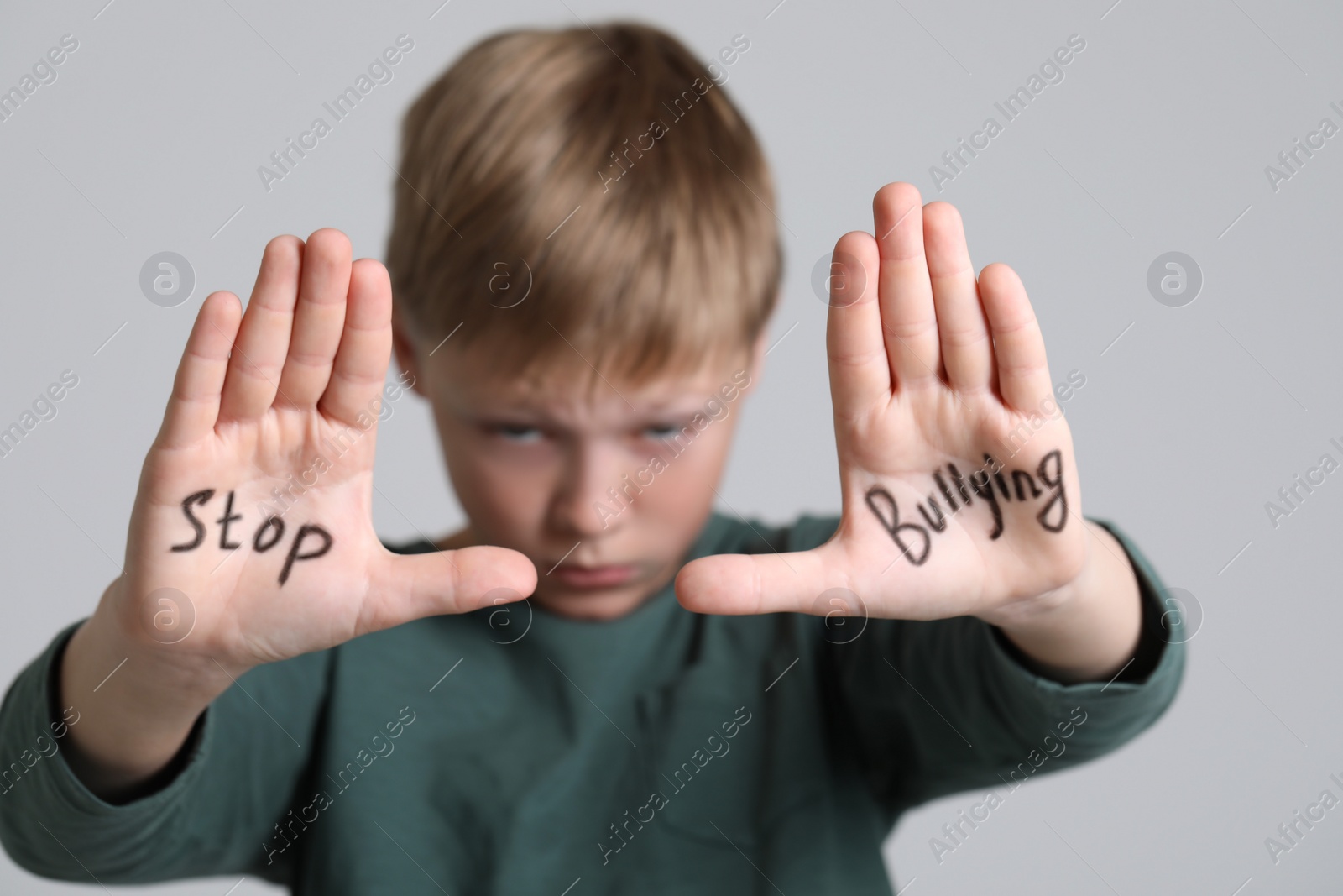 Photo of Boy showing hands with phrase Stop Bullying on light grey background, selective focus