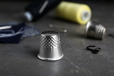 Photo of Silver sewing thimble on grey table, closeup. Space for text