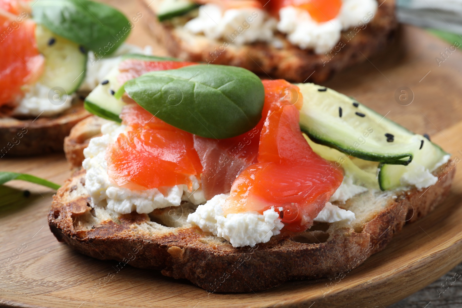 Photo of Delicious sandwich with cream cheese, salmon, cucumber and spinach on wooden plate, closeup