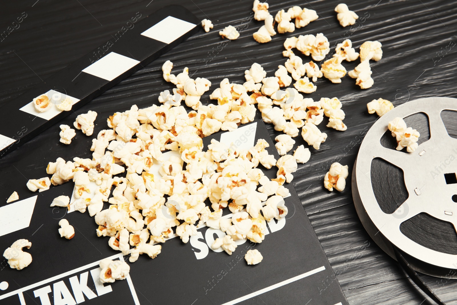 Photo of Tasty popcorn, film reel and clapperboard on wooden table. Cinema snack