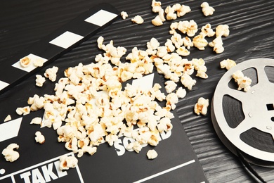 Tasty popcorn, film reel and clapperboard on wooden table. Cinema snack