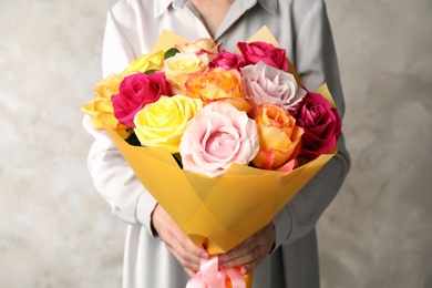 Photo of Woman holding luxury bouquet of fresh roses on beige background, closeup