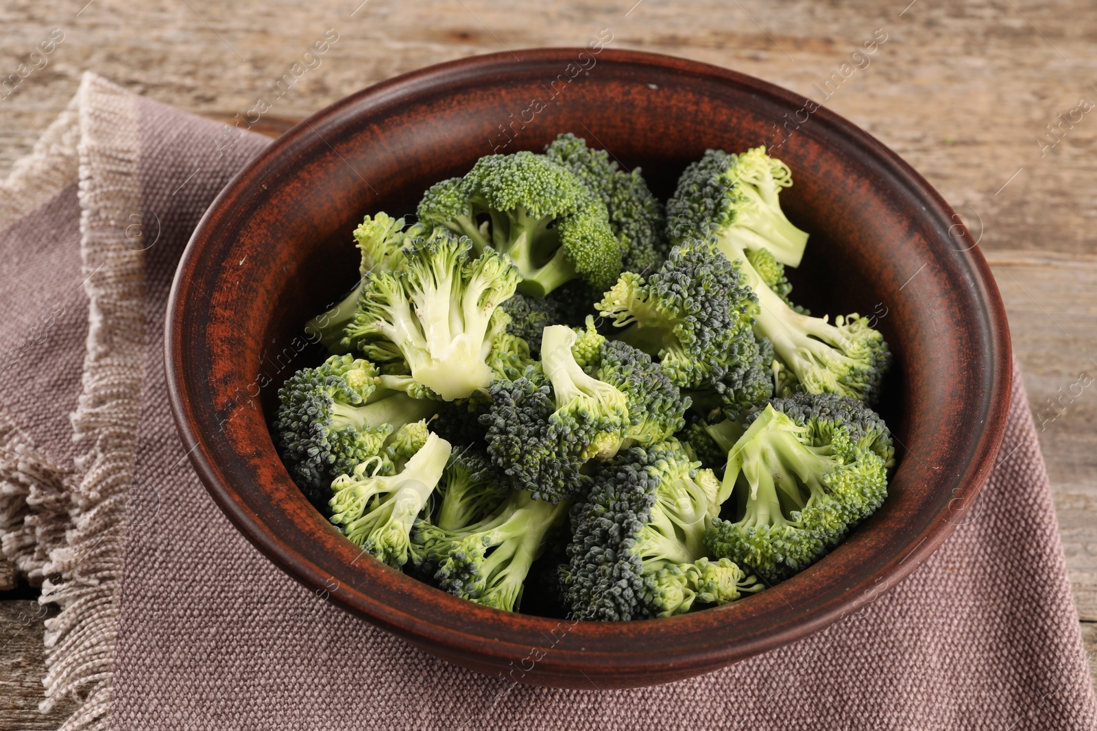 Photo of Bowl with fresh raw broccoli on wooden table, closeup