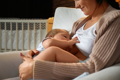 Photo of Woman breast feeding her baby at home, closeup