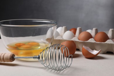 Photo of Metal whisk and raw eggs on light table, closeup