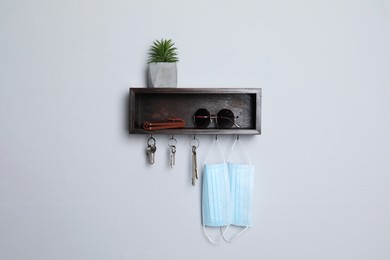 Photo of Wooden hanger for keys with wallet, sunglasses, medical masks and houseplant on white wall