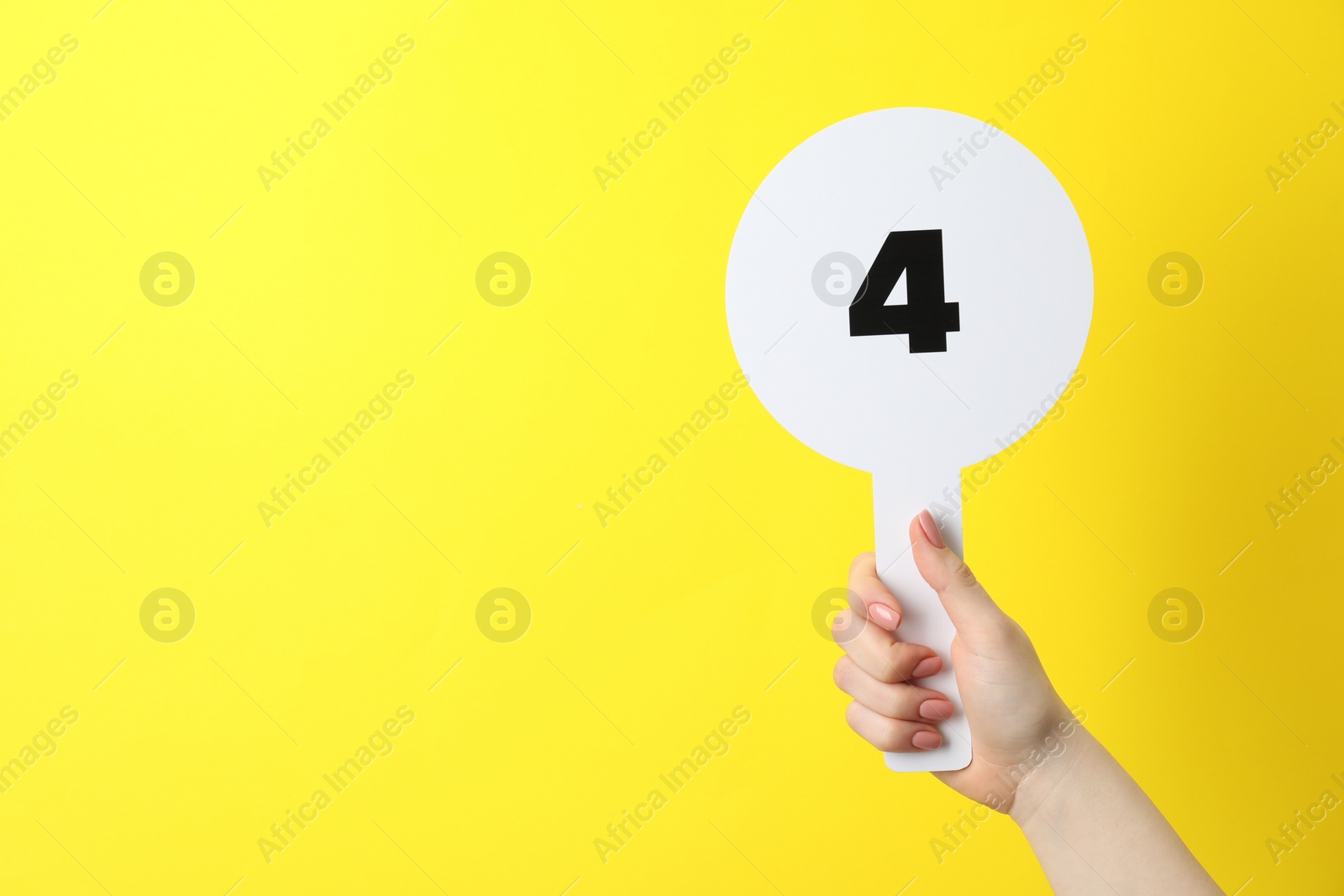 Photo of Woman holding auction paddle with number 4 on yellow background, closeup. Space for text