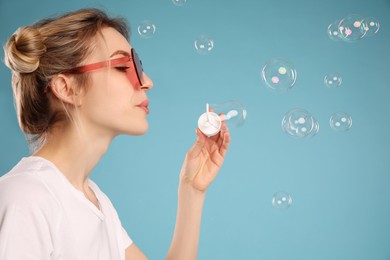 Photo of Young woman blowing soap bubbles on light blue background, space for text