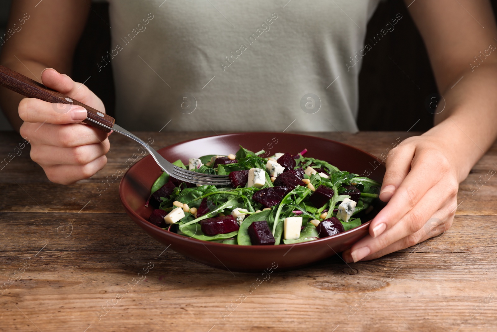 Photo of Woman eating fresh delicious beet salad at wooden table, closeup