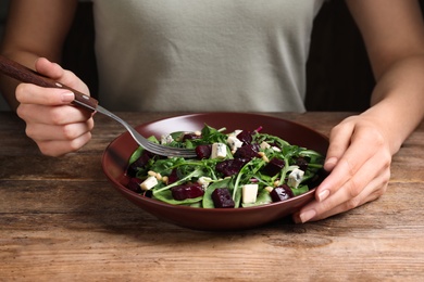 Photo of Woman eating fresh delicious beet salad at wooden table, closeup