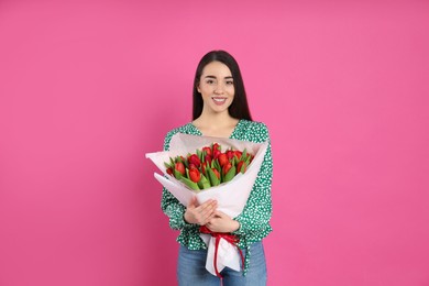 Happy woman with red tulip bouquet on pink background. 8th of March celebration