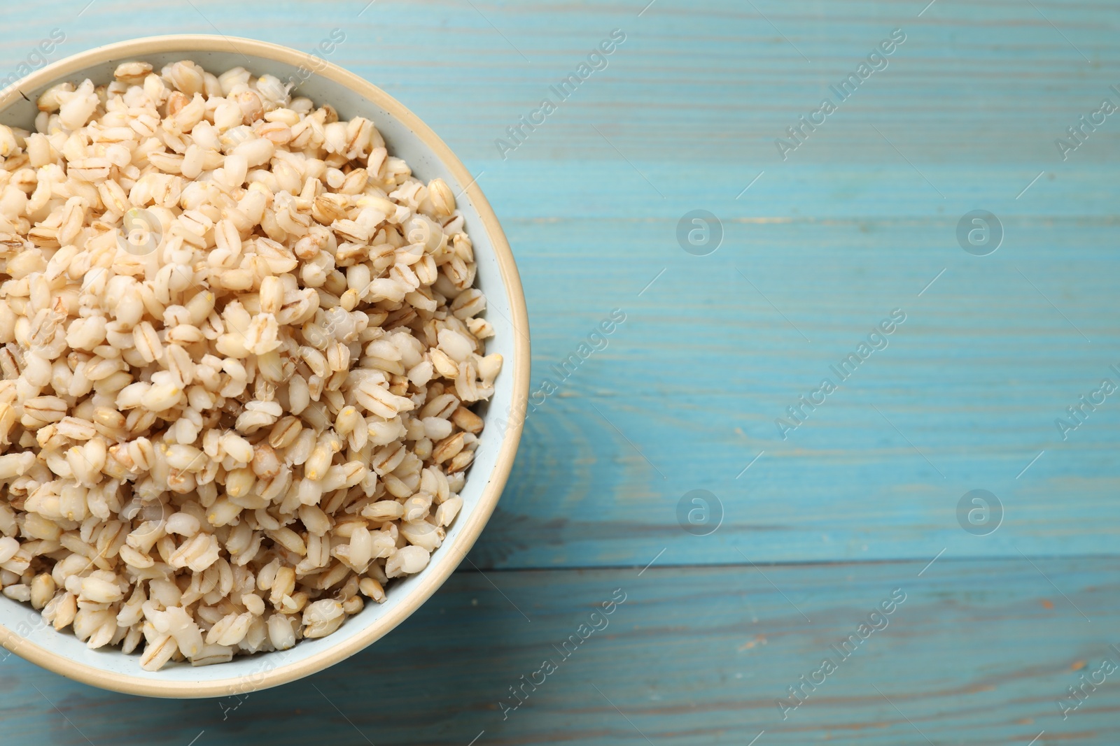 Photo of Delicious pearl barley in bowl on light blue wooden table, top view. Space for text