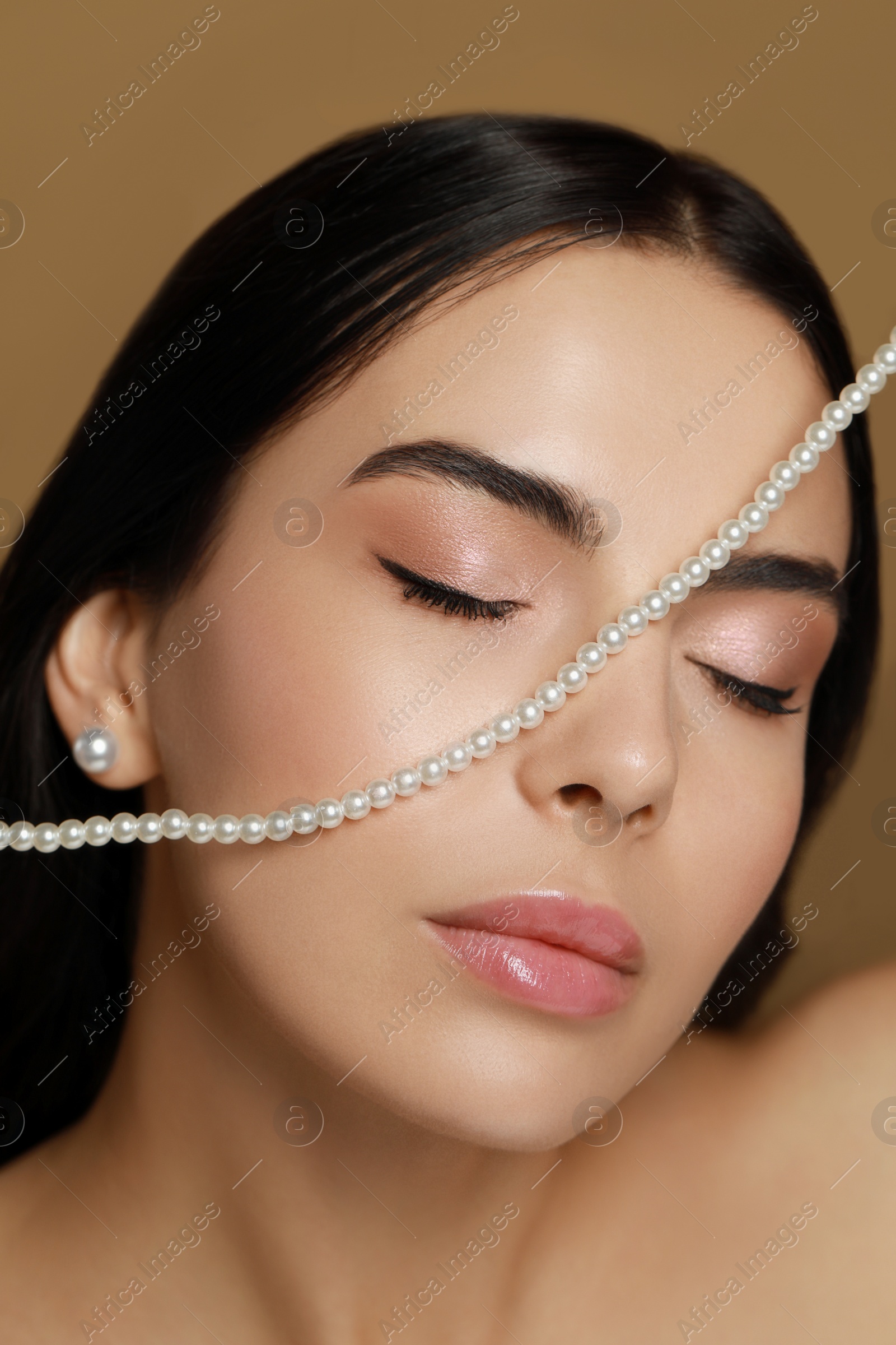 Photo of Young woman with elegant pearl jewelry on brown background, closeup