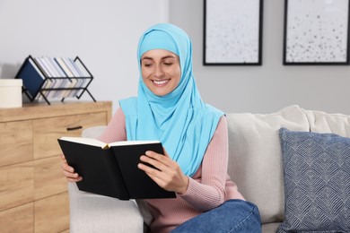 Muslim woman reading book on couch in room