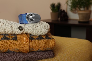 Photo of Modern fabric shaver and knitted clothes on orange blanket indoors, closeup. Space for text