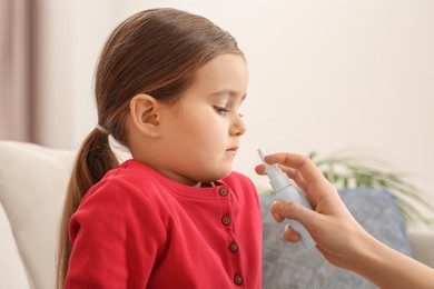Photo of Mother using nasal spray to treat her little daughter on sofa indoors, closeup