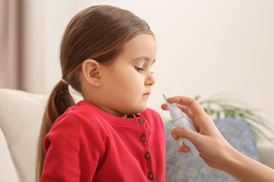 Mother using nasal spray to treat her little daughter on sofa indoors, closeup