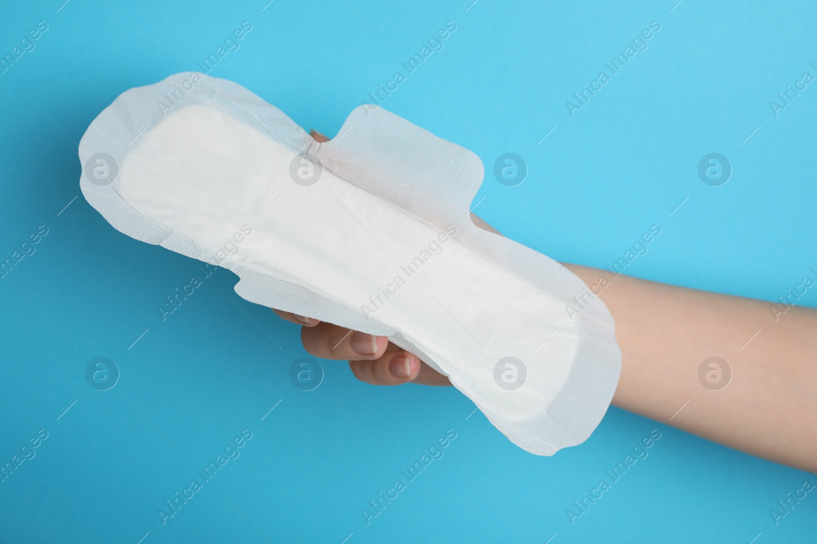 Photo of Woman holding sanitary napkin on light blue background, closeup