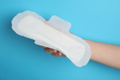 Woman holding sanitary napkin on light blue background, closeup