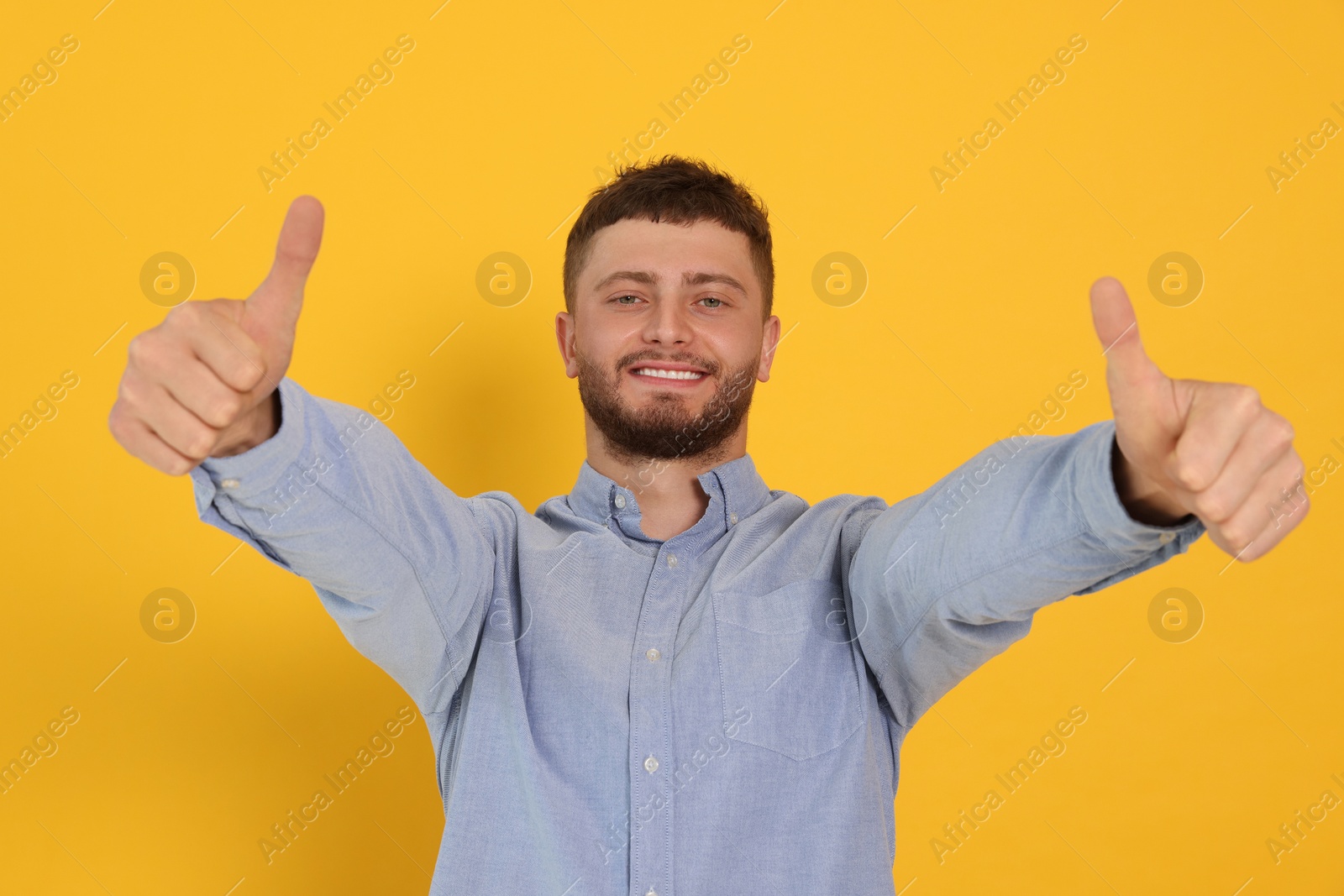 Photo of Young man showing thumbs up on orange background