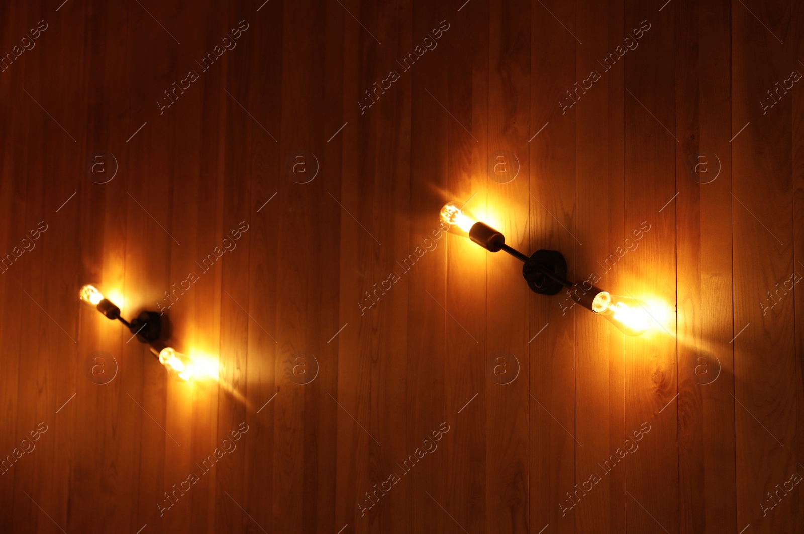 Photo of Lamps with glowing light bulbs on wooden wall indoors