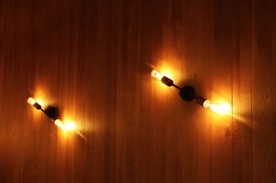 Lamps with glowing light bulbs on wooden wall indoors