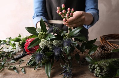 Photo of Florist making beautiful bouquet with fresh flowers at wooden table, closeup