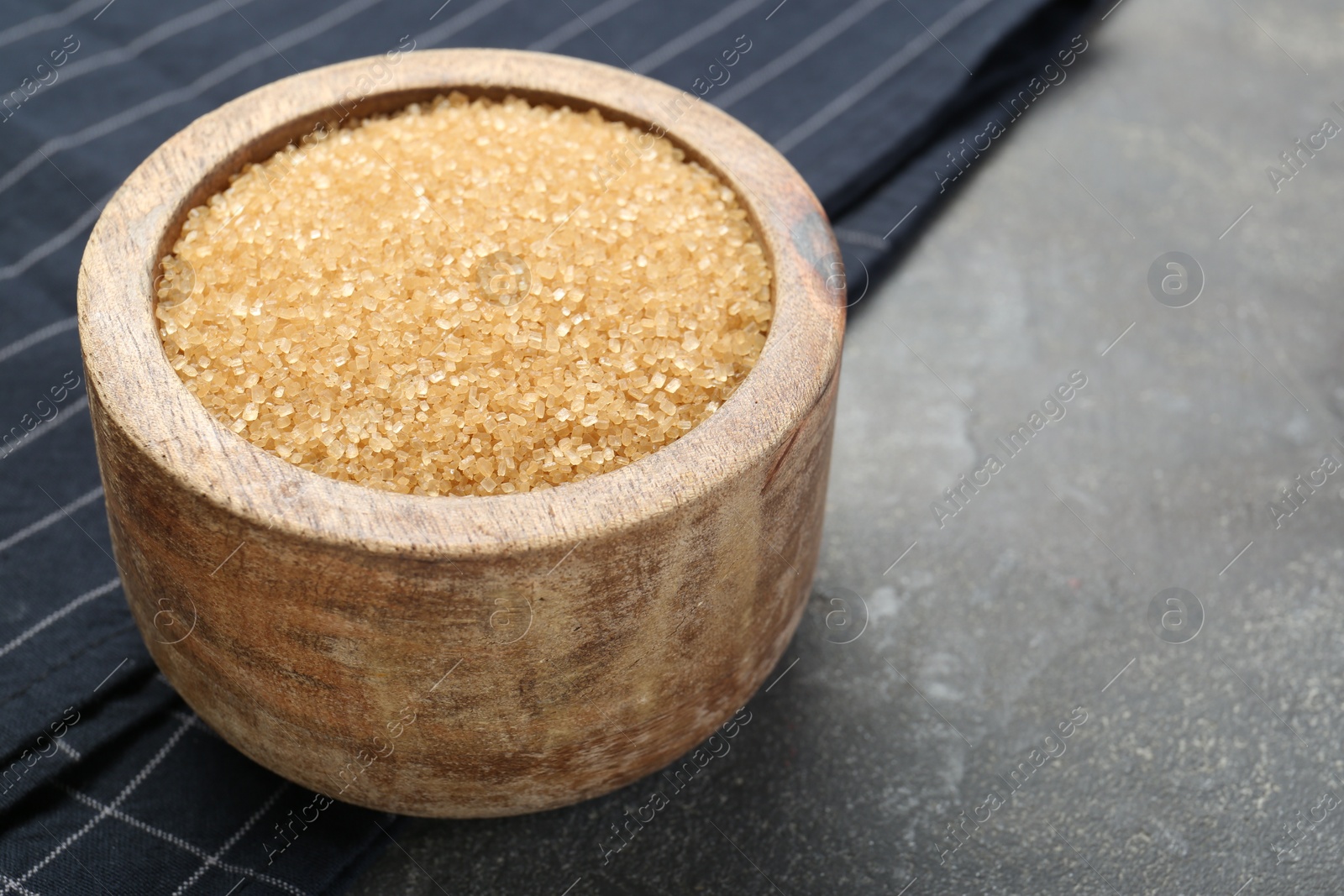 Photo of Brown sugar in bowl on grey textured table, closeup. Space for text