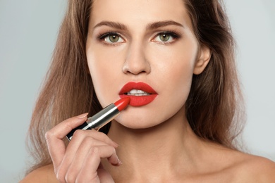 Photo of Young woman applying red lipstick on gray background