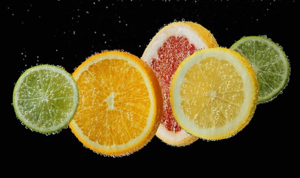 Photo of Slices of different citrus fruits in sparkling water on black background