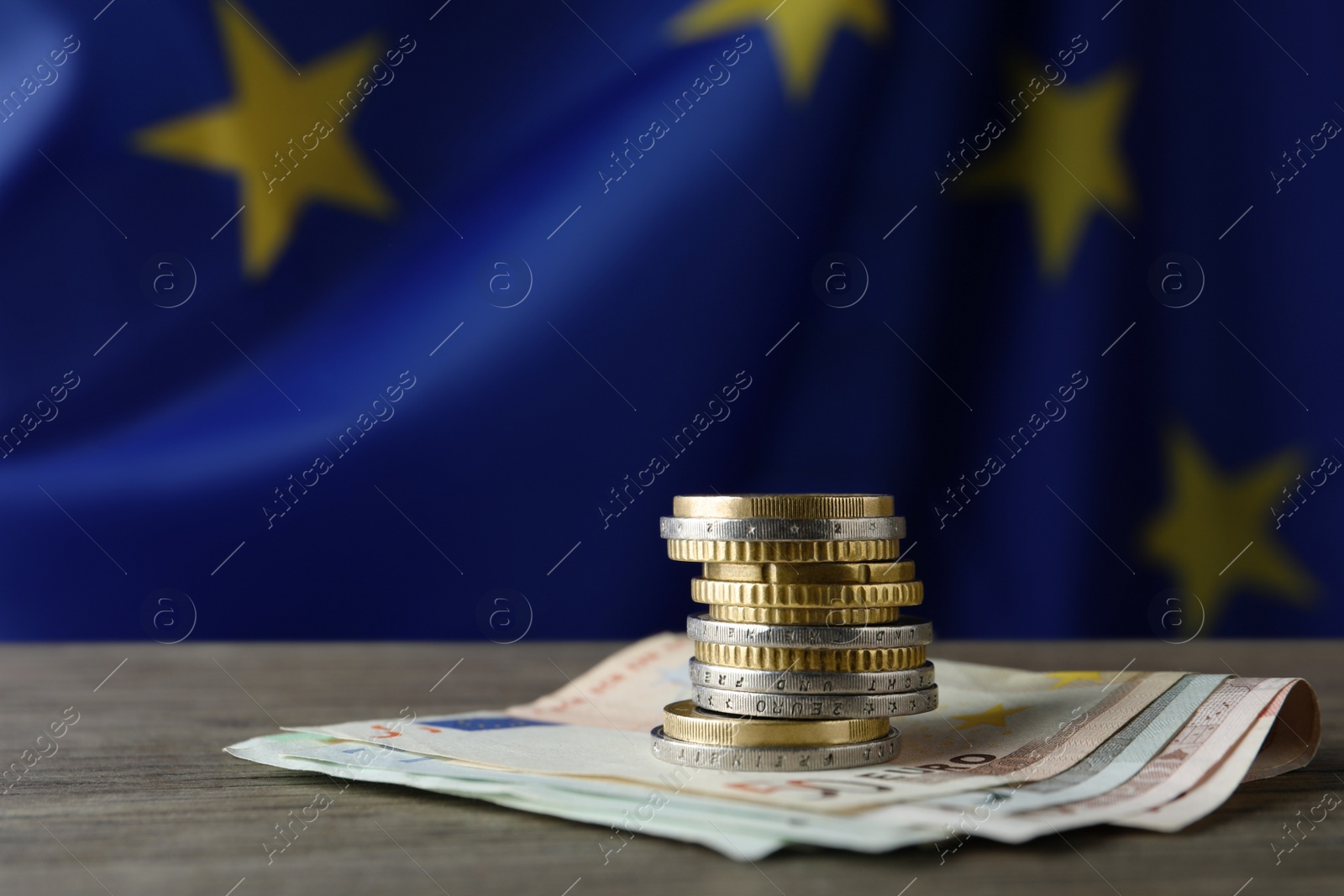 Photo of Stack of coins and banknotes on wooden table against European Union flag, space for text