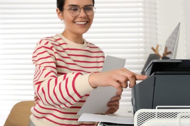 Woman using modern printer at workplace indoors, selective focus