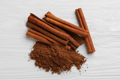 Photo of Dry aromatic cinnamon sticks and powder on white wooden table, top view