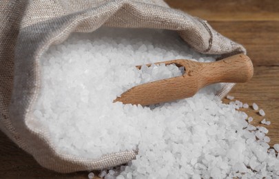 Photo of Bag of natural sea salt and scoop on wooden table, closeup