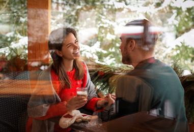 Lovely couple at table in cafe, view through window. Winter vacation