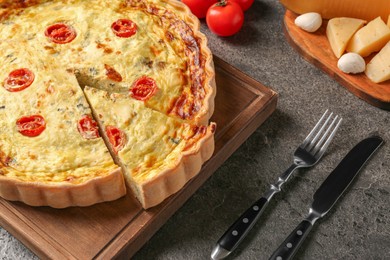 Photo of Delicious homemade cheese quiche, cutlery and ingredients on gray table