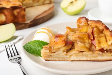 Slice of traditional apple pie with ice cream and mint on white table, closeup