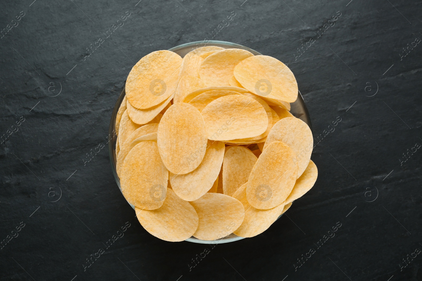 Photo of Bowl with delicious potato chips on black table, top view