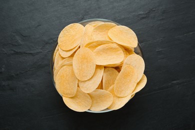 Bowl with delicious potato chips on black table, top view