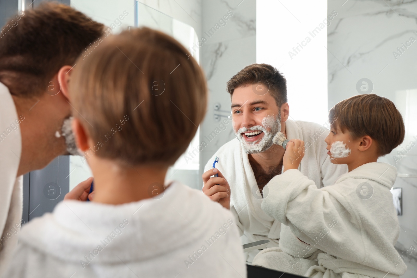 Photo of Dad and son with shaving foam on their faces having fun in bathroom