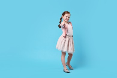 Photo of Cute little girl dancing on light blue background, space for text