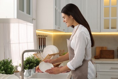 Photo of Happy woman washing plate at sink in kitchen