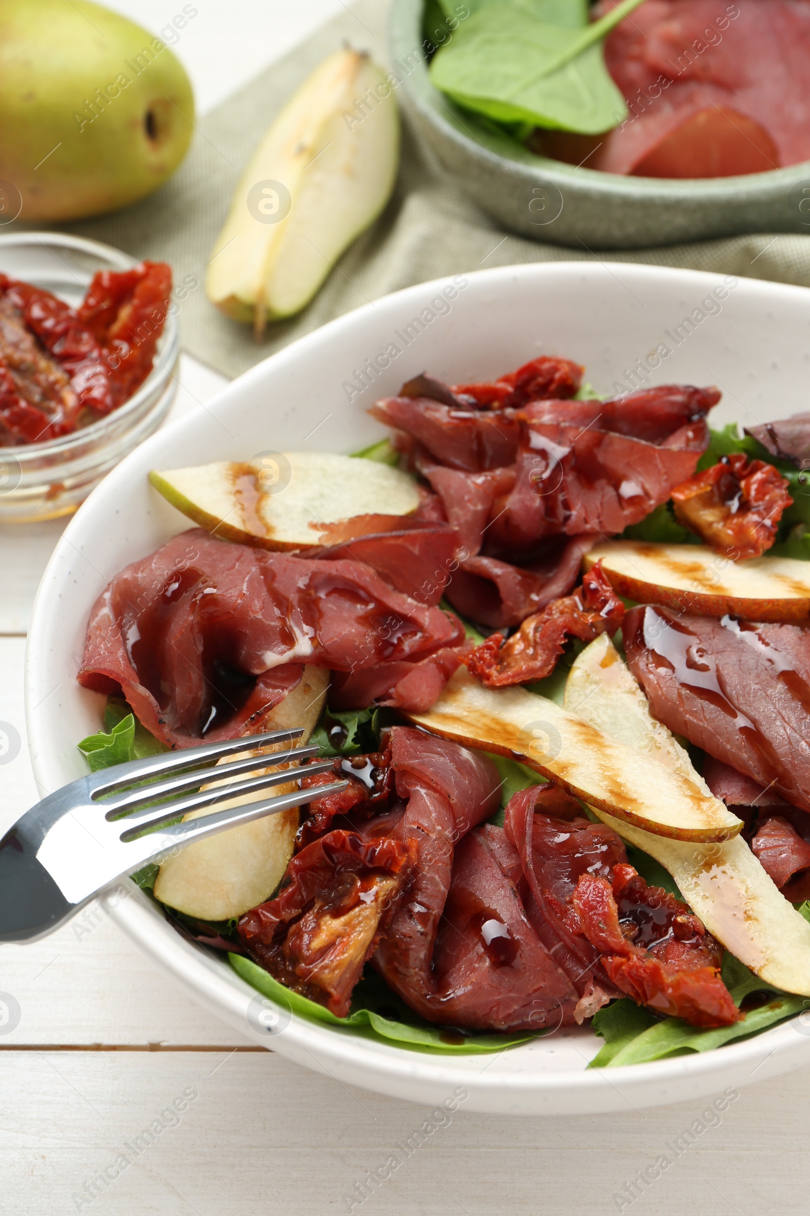 Photo of Delicious bresaola salad with sun-dried tomatoes, pears and balsamic vinegar served on white wooden table, closeup