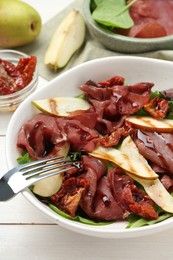 Delicious bresaola salad with sun-dried tomatoes, pears and balsamic vinegar served on white wooden table, closeup