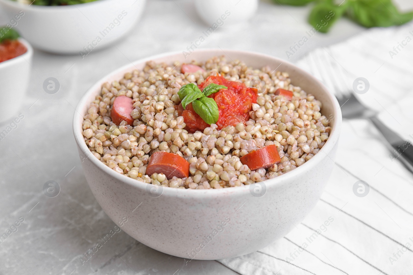 Photo of Tasty buckwheat porridge with sausages on grey marble table