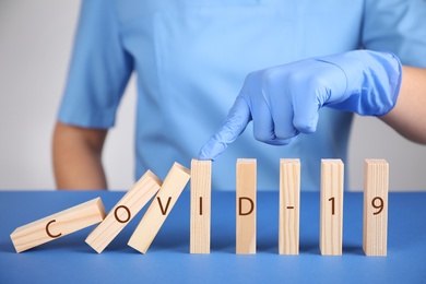 Photo of Doctor stopping domino effect at blue table, closeup. Prevent spreading of coronavirus