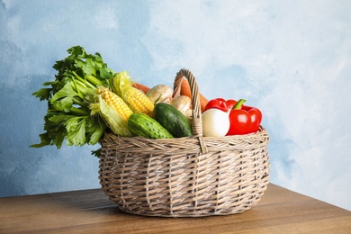 Photo of Basket full of fresh healthy vegetables on table against color background